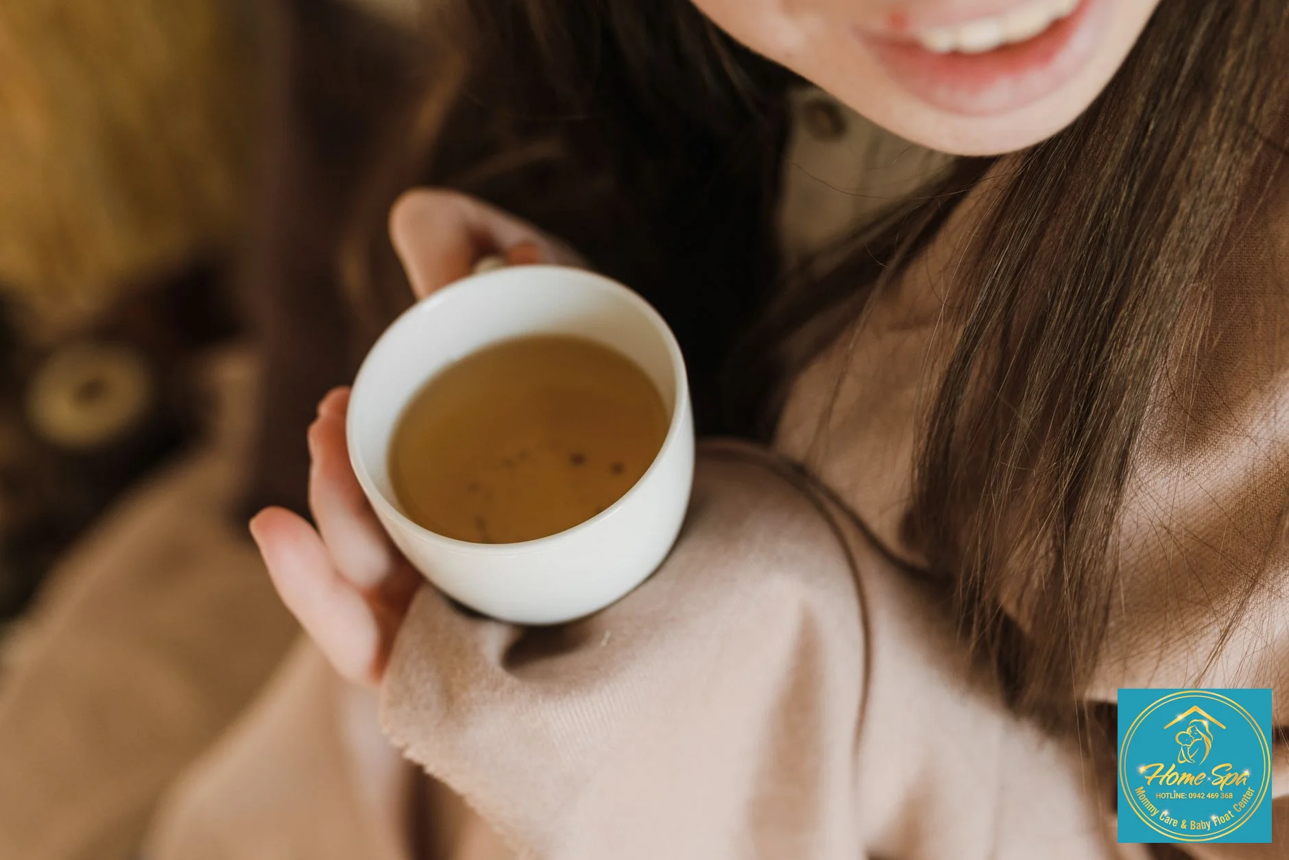A young mother drinking a cup of herbal tea, looking relaxed and healthy, with a baby in a soft carrier, natural lighting, 1024x1024